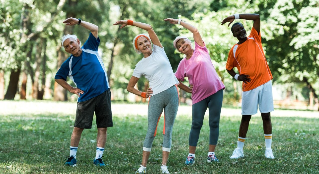 Multiracial group of older adults smiling and doing outdoor stretching exercises on the grass.