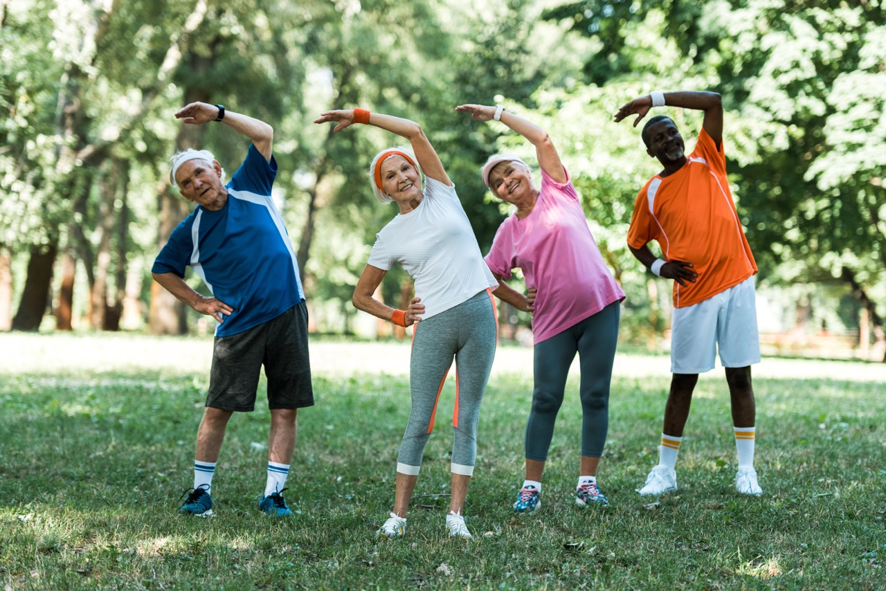 Multiracial group of older adults smiling and doing outdoor stretching exercises on the grass.