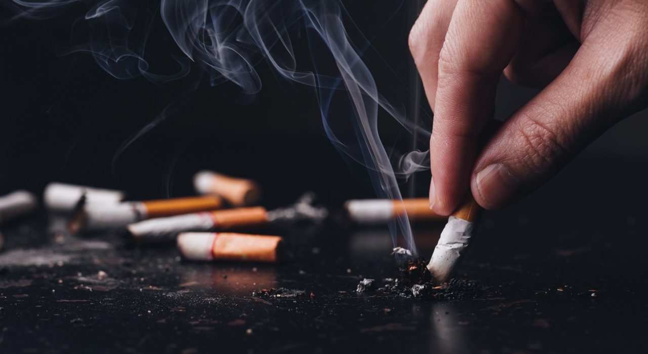 Close-up of a person holding a lit cigarette, illustrating the connection between tobacco use and vascular health risks.