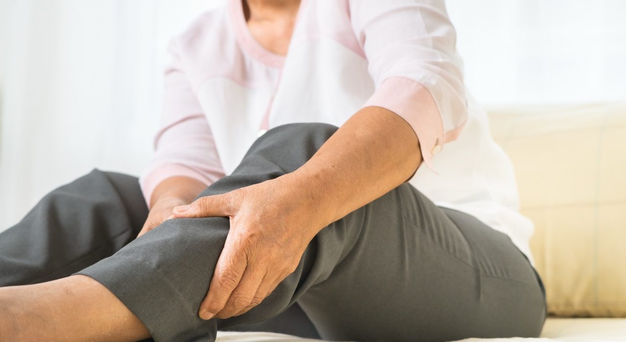 Senior woman holding her leg in pain while sitting at home, illustrating potential circulation issues or leg discomfort.