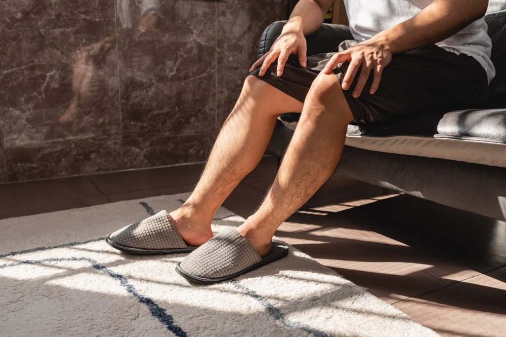 A close-up shot of a person relaxing at home in casual slippers, focusing on legs and feet to illustrate leg comfort and wellness.