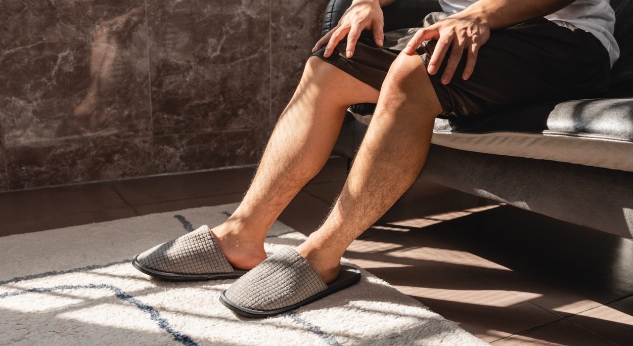 A close-up shot of a person relaxing at home in casual slippers, focusing on legs and feet to illustrate leg comfort and wellness.