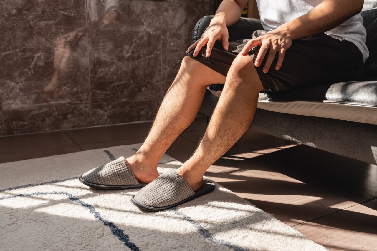 A close-up shot of a person relaxing at home in casual slippers, focusing on legs and feet to illustrate leg comfort and wellness.