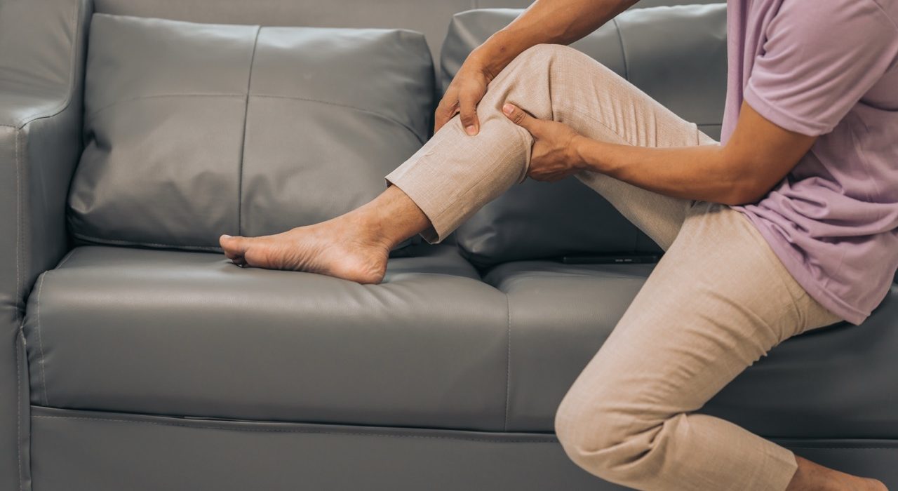 Middle-aged man sitting on a sofa while clutching his painful leg