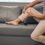 Middle-aged man sitting on a sofa while clutching his painful leg